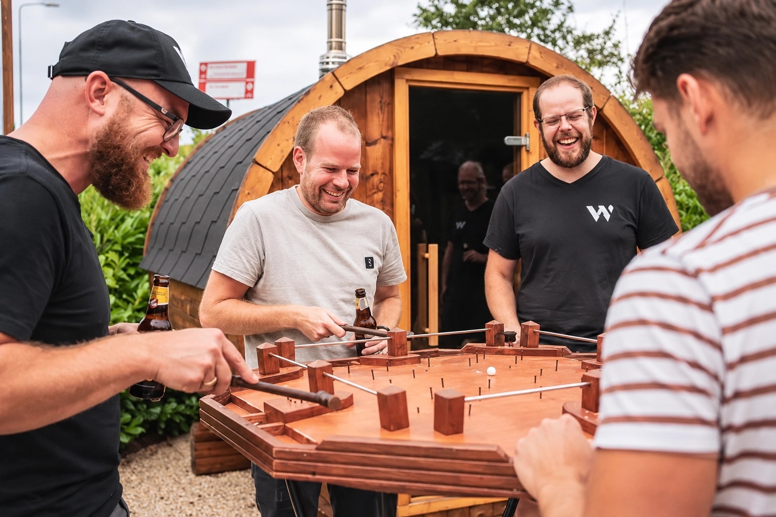 Vier collega's lachen om het hamerspel tijdens een bedrijfsuitje bij een houten sauna