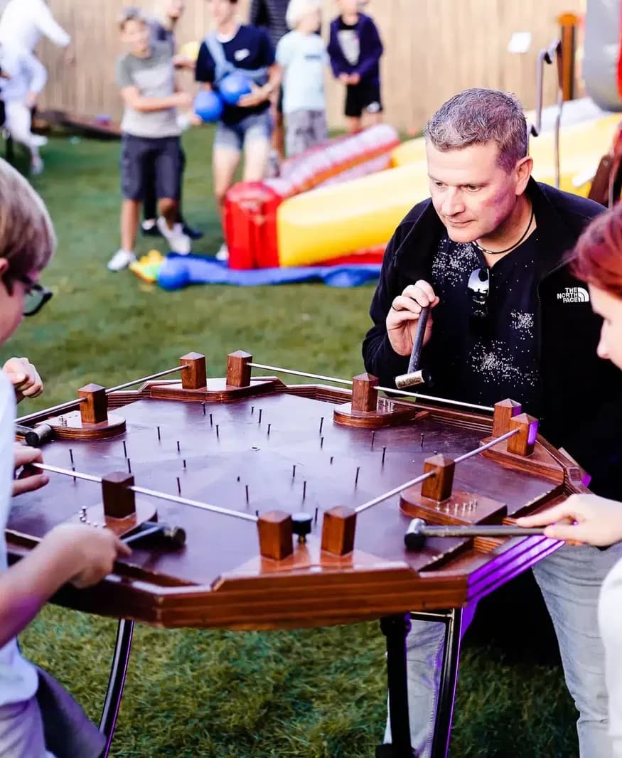 Man en kinderen met hamers aan het hamerspel, met een springkussen erachter