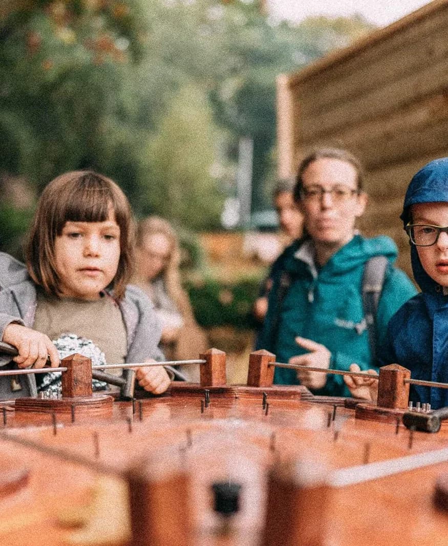 Meisje kijkt over de spijkers van het hamerspel, met haar familie erachter