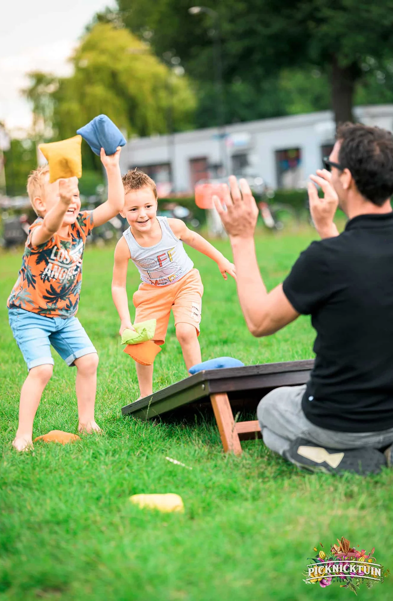 Kinderen gooien zakjes bij cornhole terwijl hun vader aanwijst