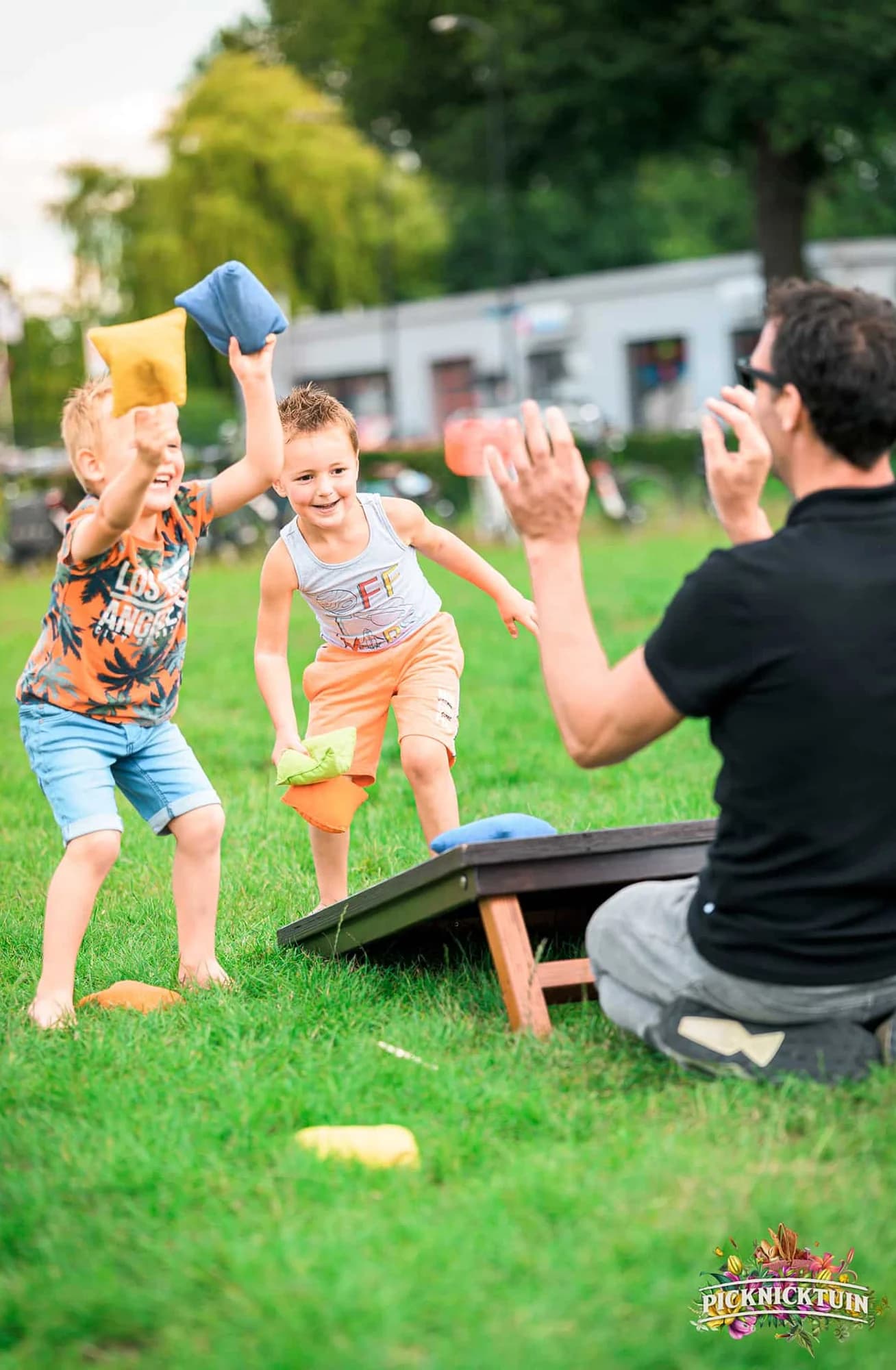 Kinderen gooien zakjes bij cornhole terwijl hun vader aanwijst